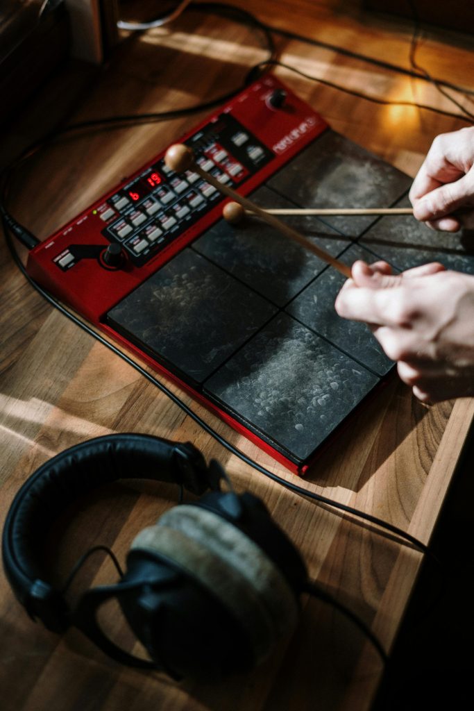Primer plano de unas manos tocando un pad de percusión electrónica con baquetas en un estudio casero.